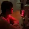 A woman using a portable red light panel while working on her computer.