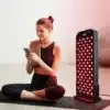 A woman using an advanced red light therapy panel, the REDi Relieve, in front of a LED light., red light therapy