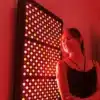 A woman posing in front of an advanced red light therapy panel., red light therapy